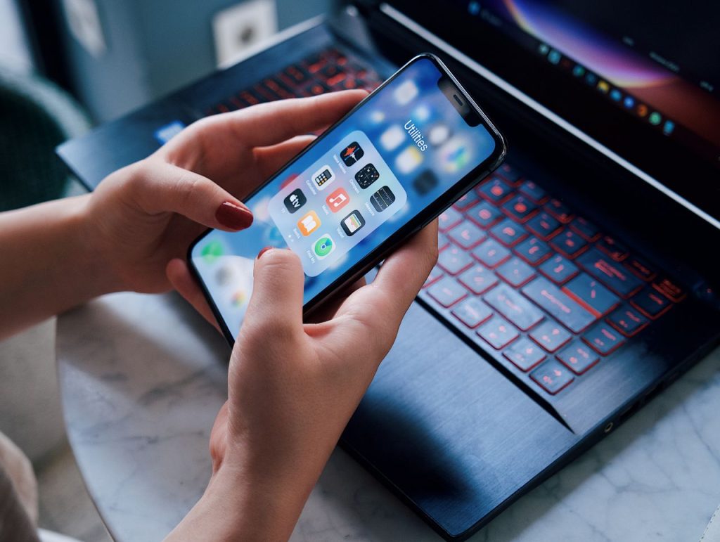Mastering the First Impression: Your intriguing post title goes here Close-up of a woman holding a smartphone showing utilities apps while sitting by a laptop indoors.